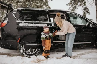 Petite fille avec sa mère devant une voiture dans un décor enneigé