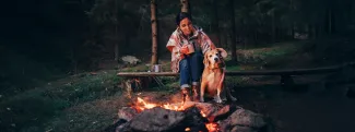 Visuel avec un chien et sa maitresse devant un feu de camp