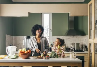 A happy mother having fun with her cute daughter while cutting vegetables