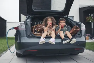 deux enfants qui croquent une pomme dans un coffre de voiture 