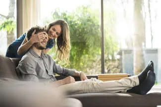 homme assis sur un canapé sa femme lui cache les yeux