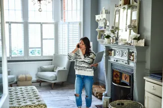 femme dans le salon d'un appartement au telephone et avec un ordinateur portable