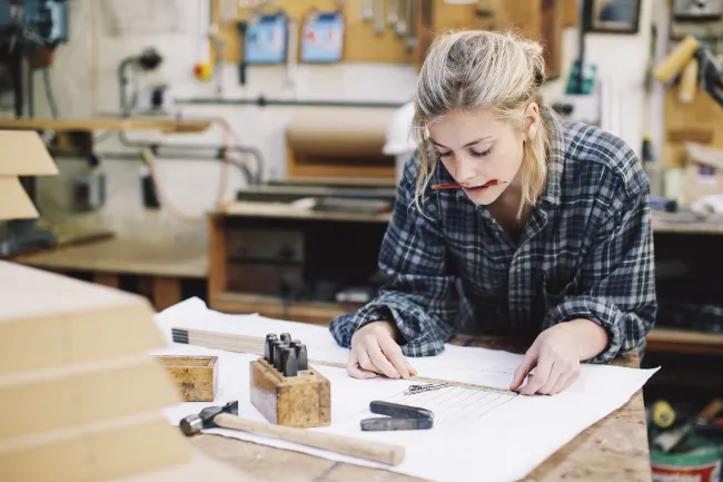 A young craftswoman measuring blueprint, placed on a workbench